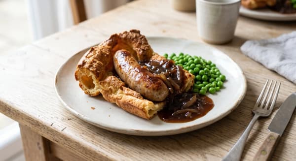 Plated toad in the hole with crisp Yorkshire pudding, sausage, onion gravy and peas