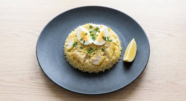 A single portion of kedgeree with spiced rice, smoked haddock flakes, two egg quarters, parsley and a lemon wedge.