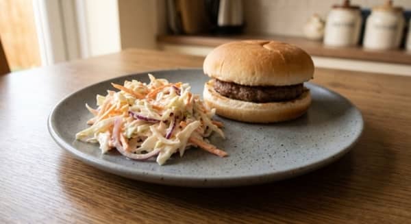 A spoonful of creamy coleslaw served beside a burger on a plate.