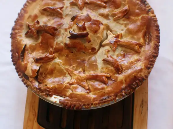 Golden puff pastry lid with steam vents over a ceramic pie dish of creamy chicken and leek pie.