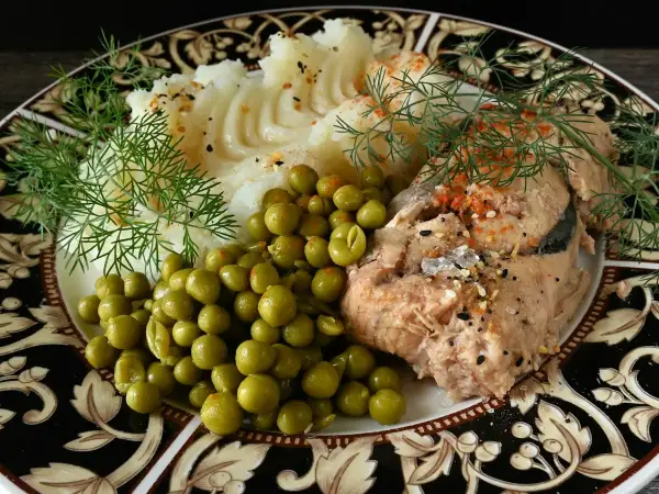 A plated portion of traditional fish pie showing creamy fish filling and golden mash with steamed peas.