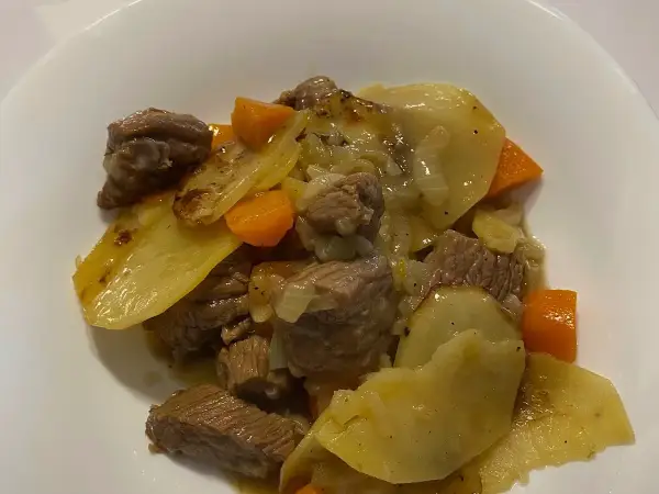 A deep bowl portion of Lancashire hotpot showing meltingly tender lamb, braised carrots and sliced potatoes in rich juices