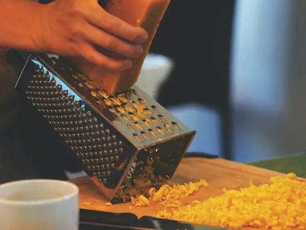 Freshly grated mature Cheddar cheese on a box grater and wooden cutting board with butter and bread for Welsh rarebit