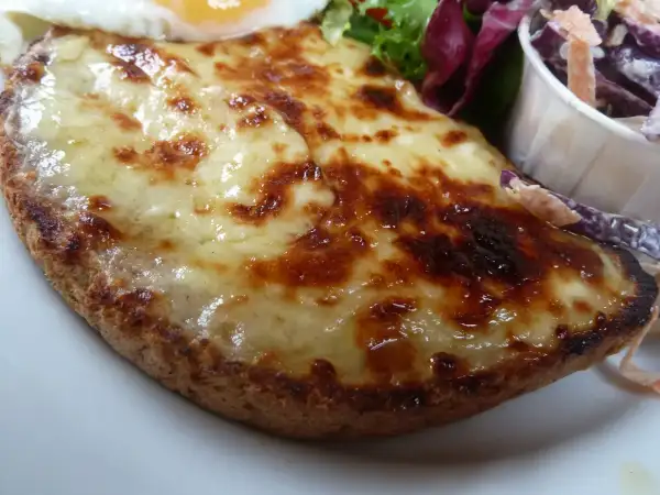A thick slice of golden grilled Welsh rarebit cut diagonally with a side salad on a white plate