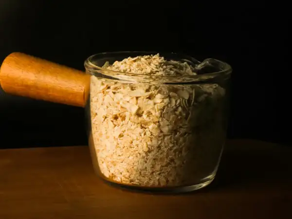 Whole rolled porridge oats in a glass bowl on a wooden board, ready for preparing overnight oats