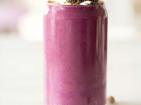 A tall glass of deep blackberry-purple smoothie with banana and yoghurt, topped with fresh blackberries