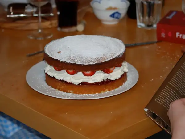 Classic two-layer golden Victoria sponge cake filled with strawberry jam and freshly whipped cream, lightly dusted with icing sugar
