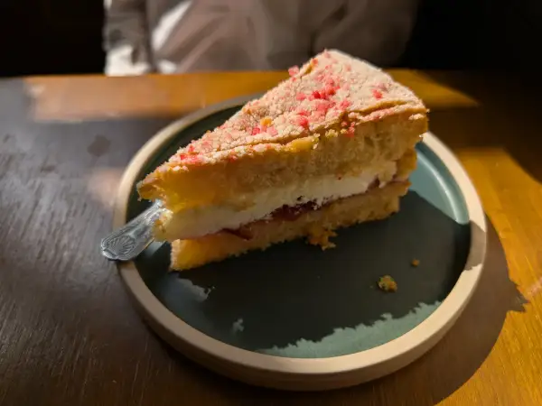 Neatly cut slice of classic Victoria sponge on a plate showing distinct layers of strawberry jam and fresh whipped cream