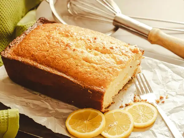 Golden rectangular lemon drizzle loaf cake on a board with delicate crunchy sugar crust, garnished with fresh lemon slices