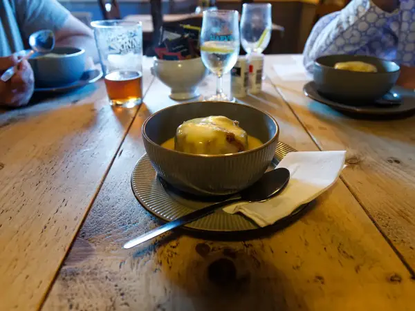 Portion of warm sticky toffee pudding on a plate with warm toffee sauce spooned over and vanilla ice cream melting alongside