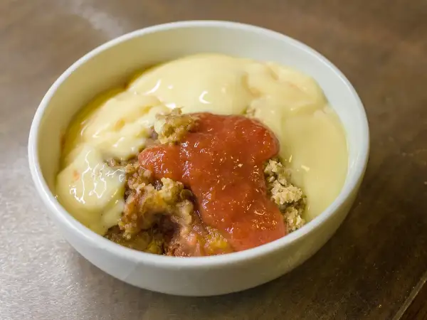 Warm serving of apple and blackberry crumble in a bowl showing purple fruit and crisp golden oat topping, served with custard