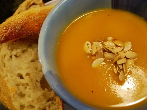Bowl of velvety roasted butternut squash soup served with crusty sourdough bread and toasted pumpkin seeds