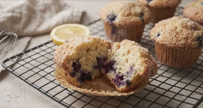 Freshly baked lemon blueberry muffins cooling on a wire rack with steaming center and crispy sugar crust