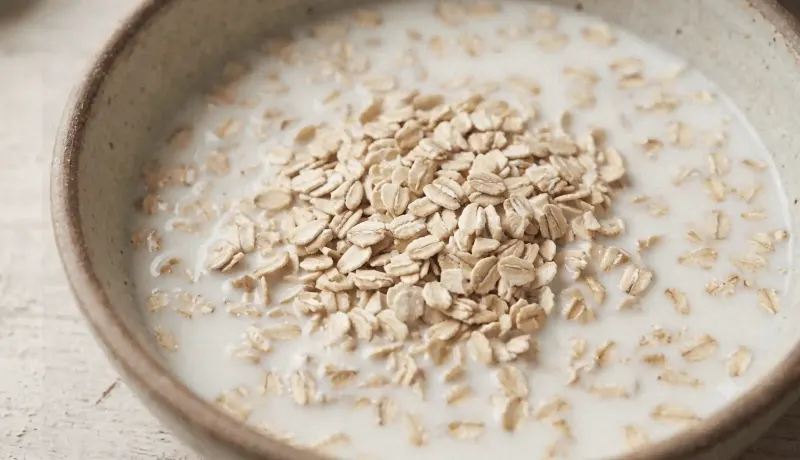 Macro shot of old-fashioned rolled oats soaking in a ceramic bowl of buttermilk, texture softening