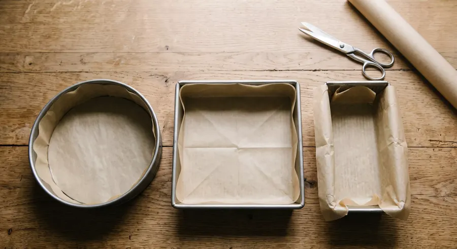 Round, square and loaf cake tins neatly lined with baking paper on a wooden worktop